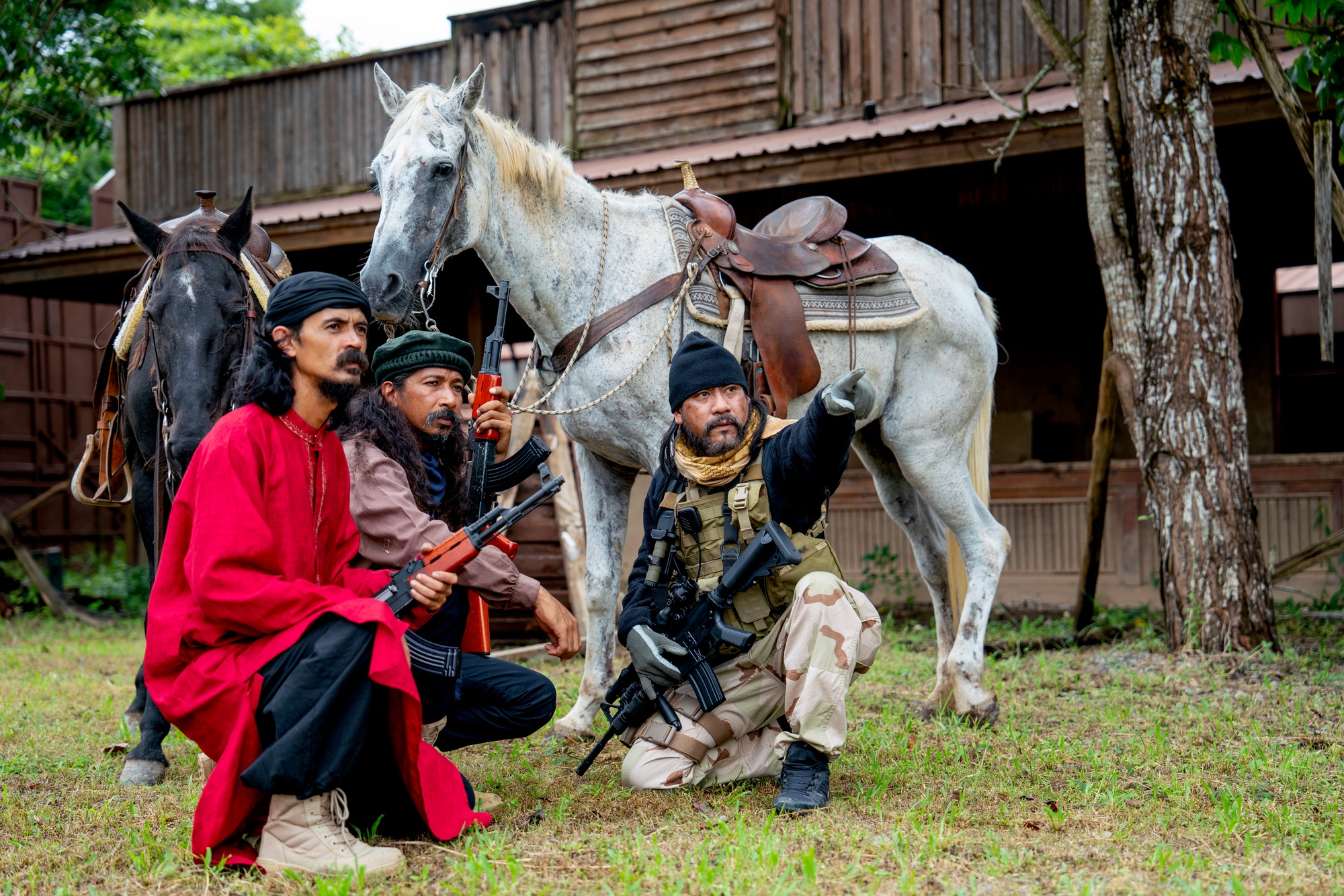 Group of men with soldier and arab clothes sit down in front of horse and old building